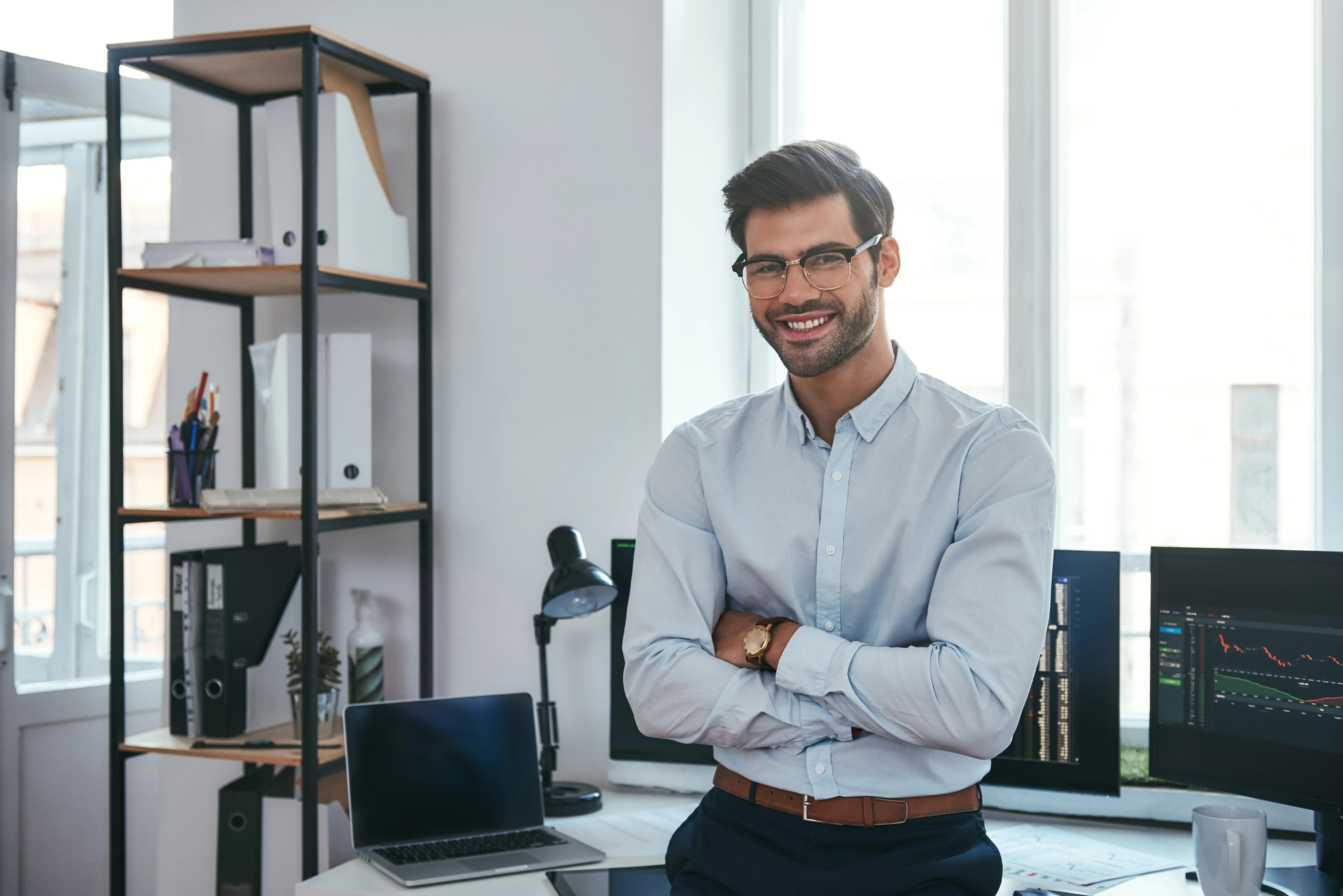 Happy trader. Cheerful businessman in formal clothes and eyeglasses is keeping arms crossed, smiling Happy trader. Cheerful businessman in formal clothes and eyeglasses is keeping arms crossed, smiling